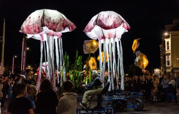 Nighttime scene of illuminated sea creatures propelled by giant pedal-powered frames