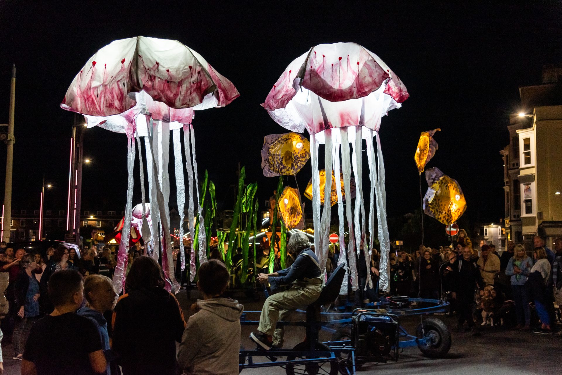 Nighttime scene of illuminated sea creatures propelled by giant pedal-powered frames
