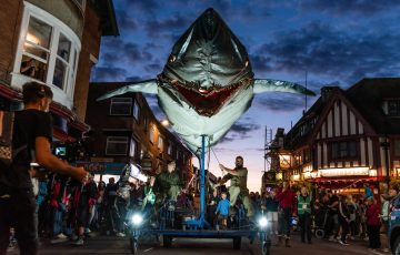 Giant pedal-powered shark puppet in amongst the smiling audience in Weymouth