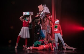Children in Christmas-themed costumes holding presents above their heads.