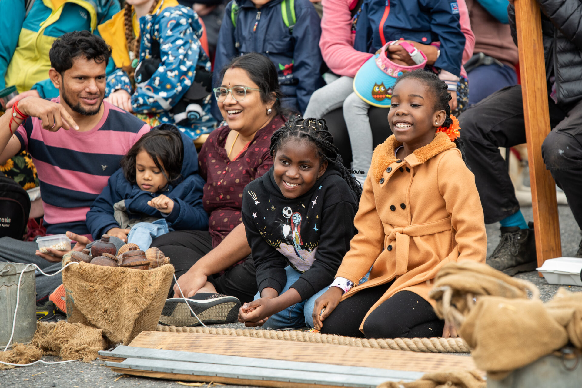 An audience wearing coasts are sat on a floor outside