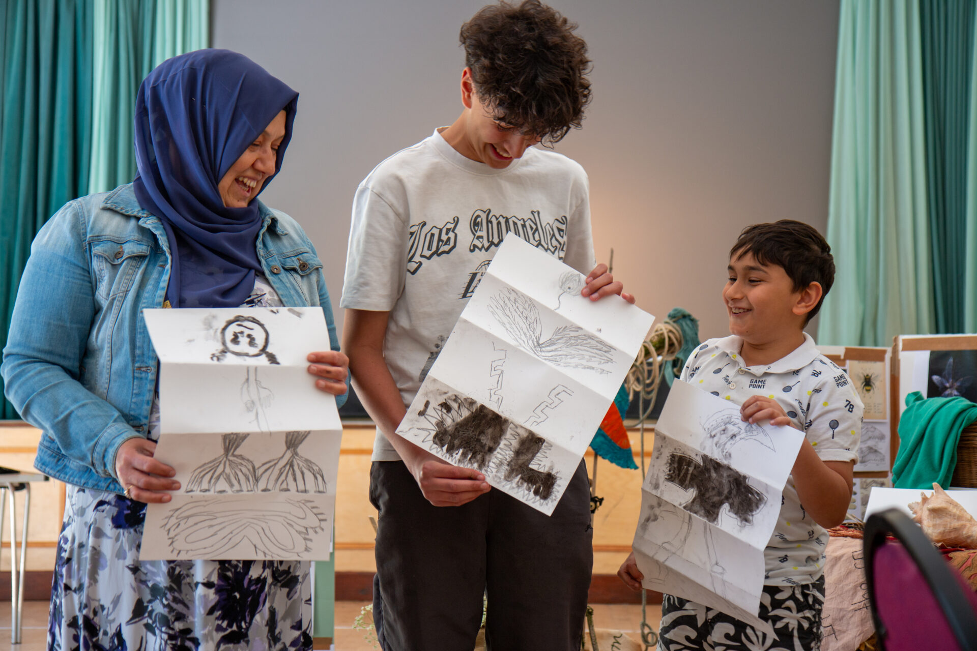 A woman and two young boys hold up their artwork proudly