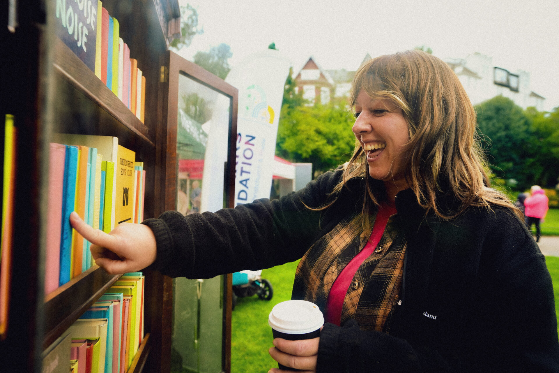 Woman pushing a book on a packed bookcase, holding a coffee cup in her left hand.