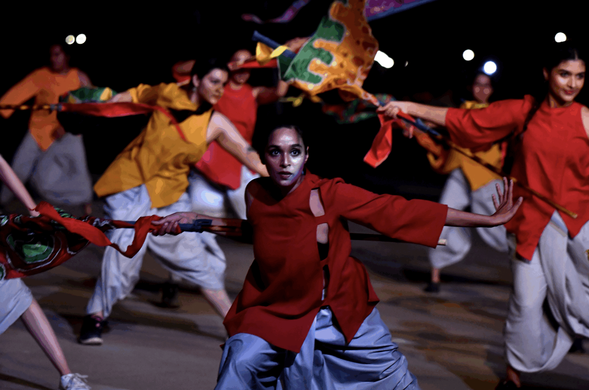 Indian dancers in red and orange costumes perform with flags