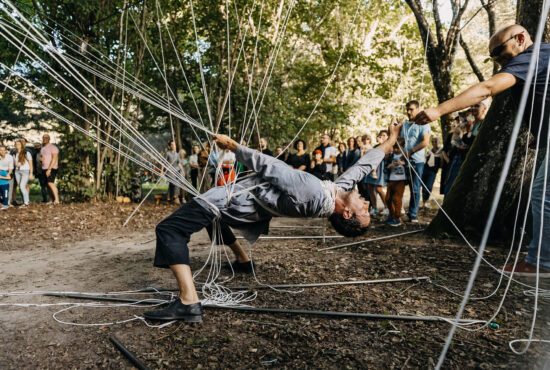 A performer bends over backwards and reaches to an audience member. They are surrounded by metal poles.