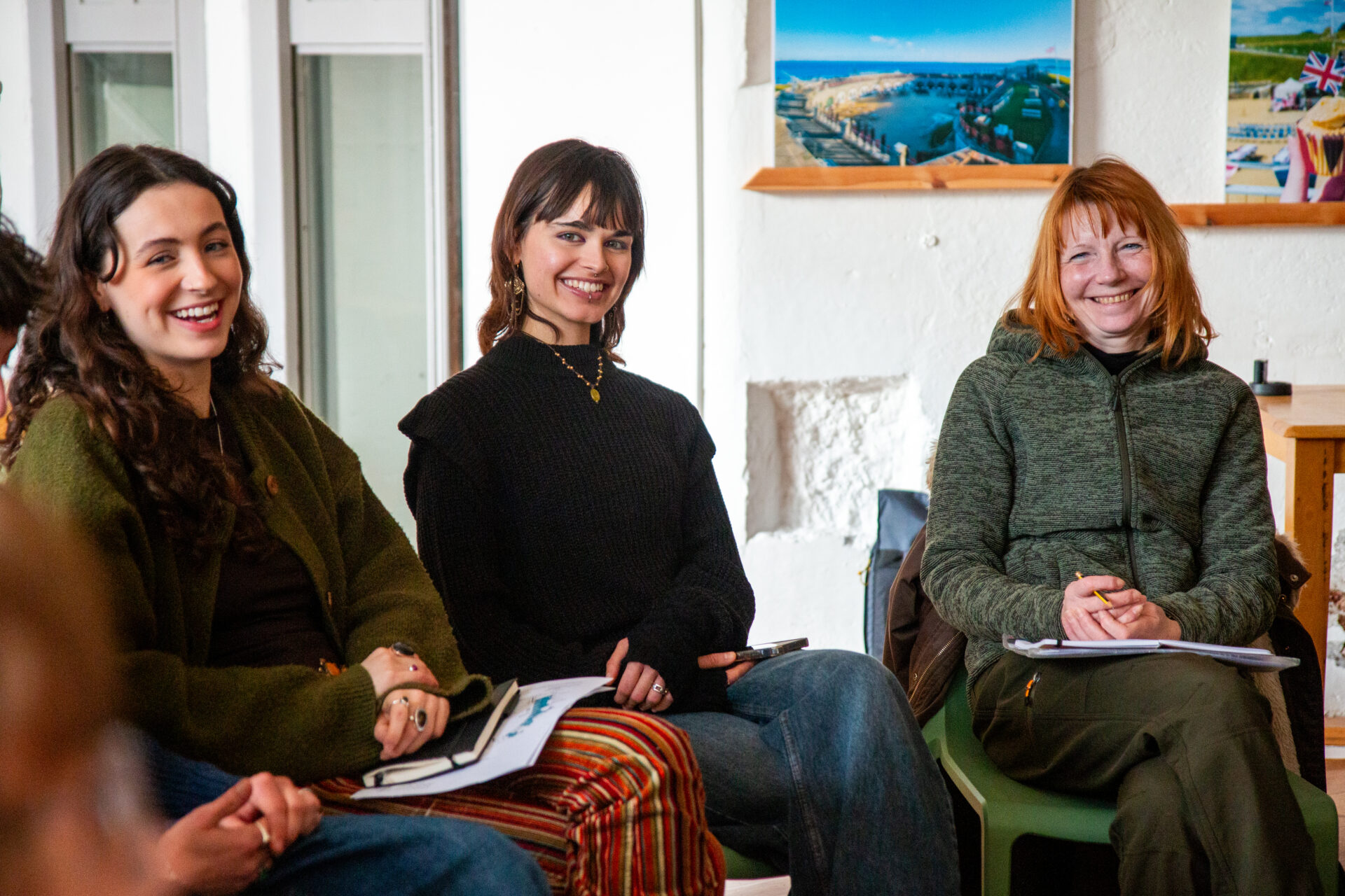 Three women sit on chairs with their legs crossed and hands in lap.