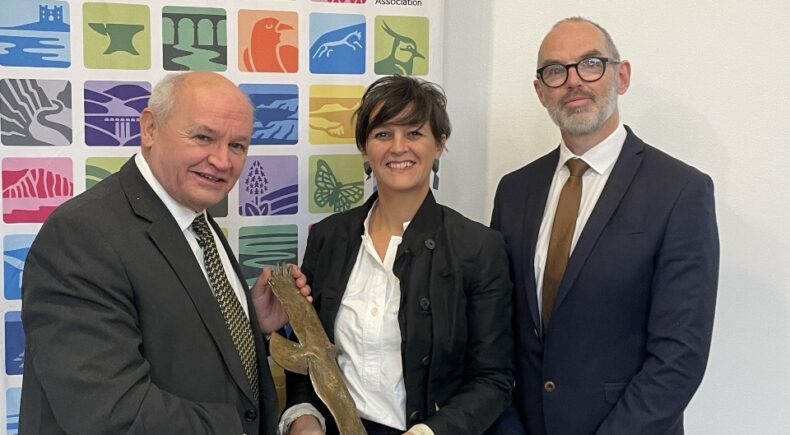 Three people post with a bronze bird award