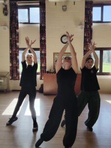 3 young female dancers hold their arms in the air with their hands crossed over.