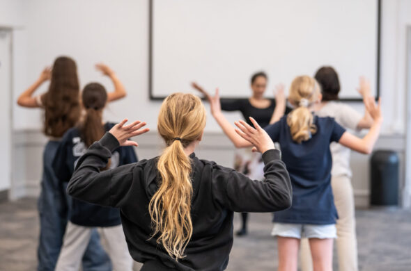 The backs of people are seen, taking part in a dance workshop