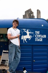 A young man poses in front of a blue trailer that says 'The Centaur Stage'