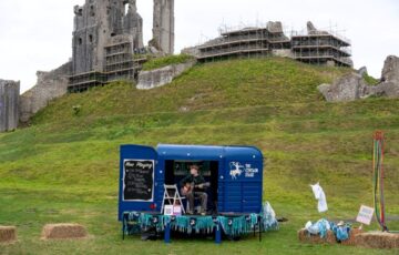 A blue trailer sits on grass in front of a large ancient castle