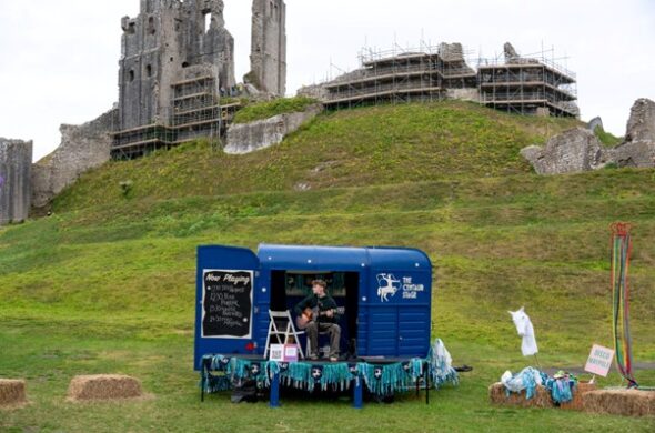 A blue trailer sits on grass in front of a large ancient castle