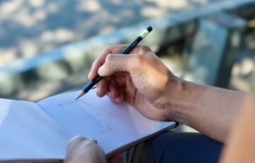 A hand holding a pencil, poised to draw on a notebook.