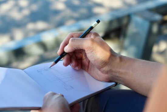 A hand holding a pencil, poised to draw on a notebook.