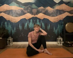 Woman in active wear posing on a yoga mat. The wall behind has mountains painted on it