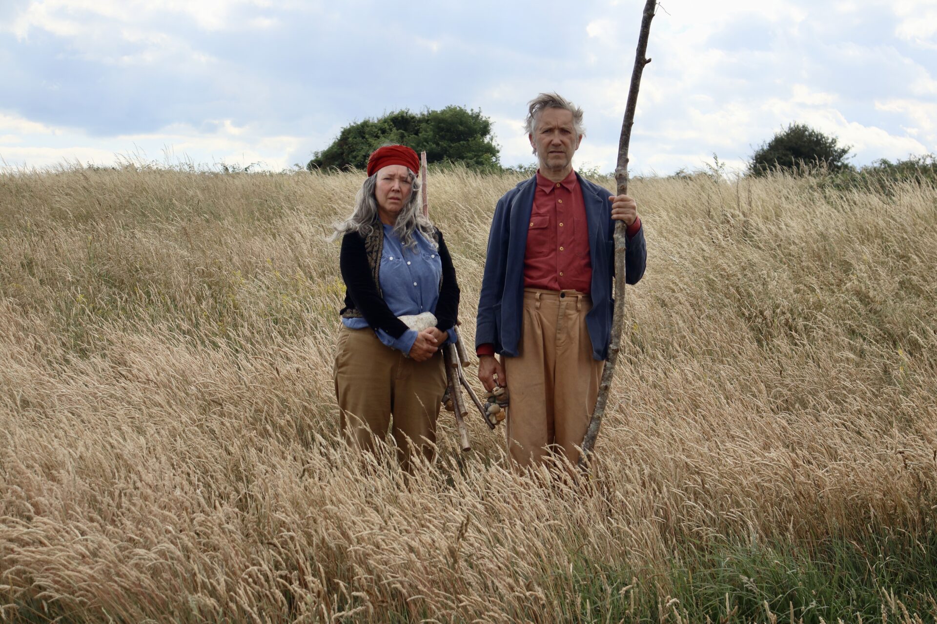 A man and woman stand in a field of long grass.