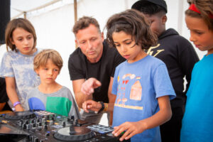 A group of children look at DJ decks, a male adult points to it.