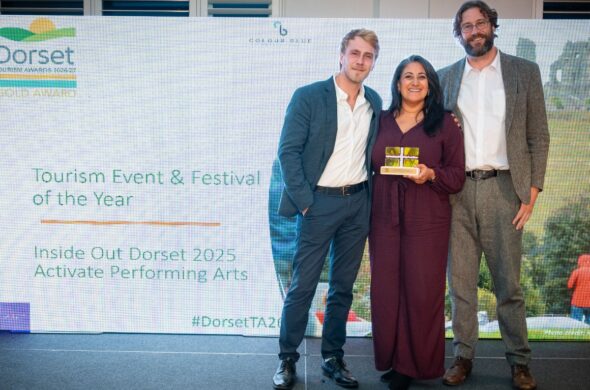 Two men and a woman holding an award stand in front of a board at an awards ceremony