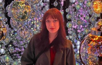 Young woman wearing a coat stands in front of lots of shining glass bulbs.