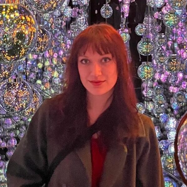 Young woman wearing a coat stands in front of lots of shining glass bulbs.